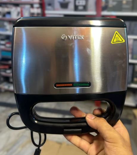 Vitek VT-7147 Sandwich Maker 750W – 4 Slice with stainless steel body held by hand showing power indicator lights and safety warning sign